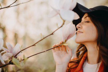A portrait of beautiful young woman and blooming tree in spring in park.