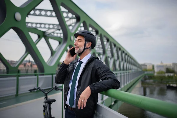 A businessman commuter on the way to work, on bridge, calling on mobile phone, sustainable lifestyle concept.