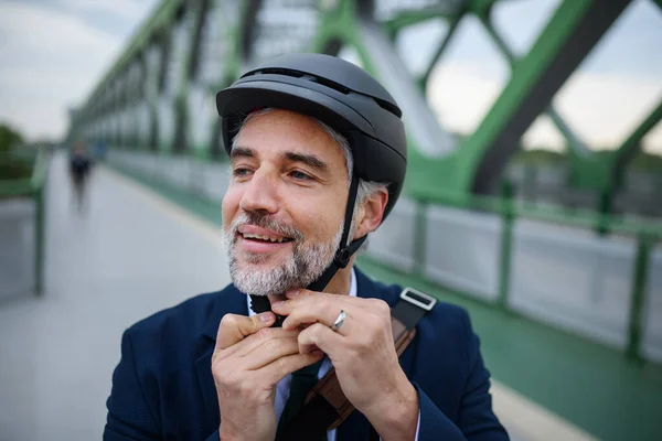 A portrait of businessman commuter on the way to work putting on cycling helmet, sustainable lifestyle concept.