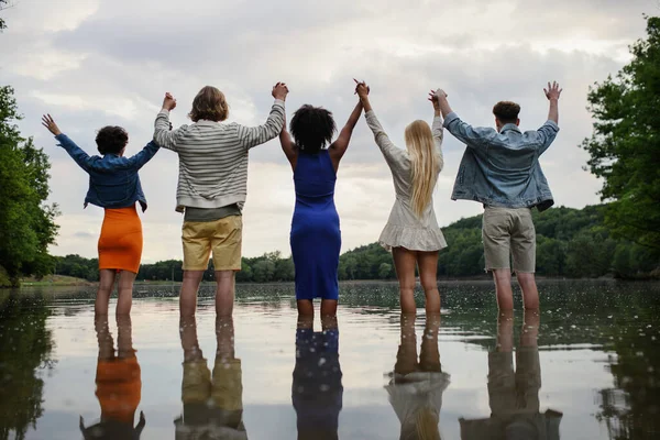 Многонациональная Группа Молодых Друзей Держащихся Руки Стоящих Летом Озере Вид — стоковое фото