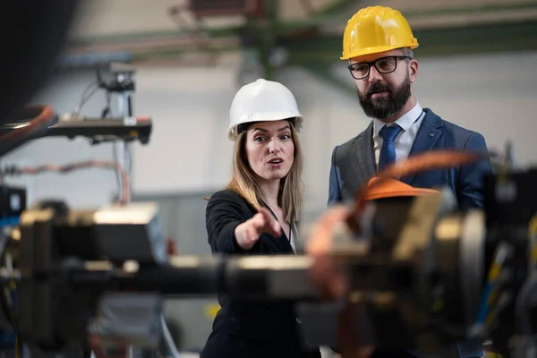 A chief engineer and project manager in modern industrial factory with robot arms talking and planning optimization of production.