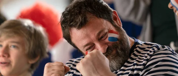 Excited football fans supproting French national team in live soccer match at astadium.