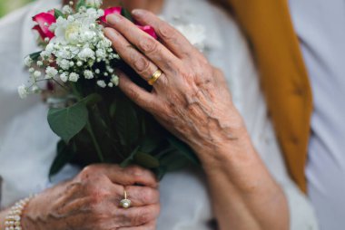 Close-up of senior hands with wedding bouquet and golden wedding rings during their marriage.