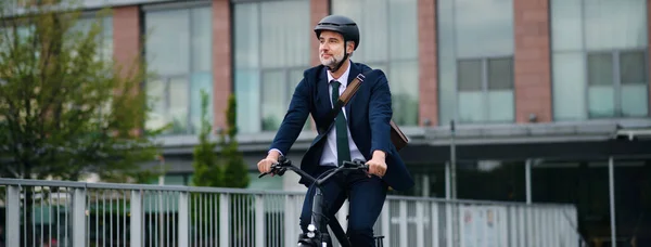 A businessman commuter on the way to work, riding bike in city, sustainable lifestyle concept. Wide photography.
