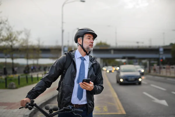 A portrait of businessman commuter on the way to work, pushing bike and using mobile phone, sustainable lifestyle concept.