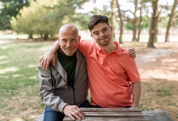 Happy Senior Father His Young Son Syndrome Embracing Sitting Park — стоковое фото