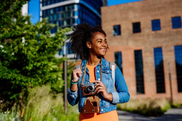 Multiracial girl walking in a city with camera, and taking photos.