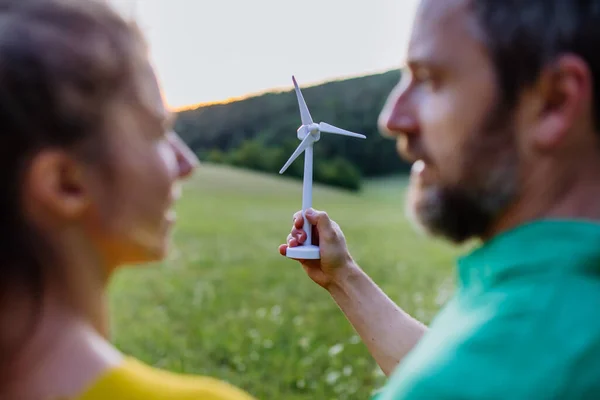 A couple standing in nature with model of wind turbine. Concept of ecology future and renewable resources.