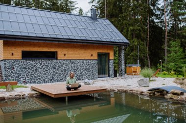 Bir kadın, dizüstü bilgisayarla çalışan, arka bahçedeki gölün kıyısında bir rıhtımda oturan, ücra bir ofis konsepti olan, tatilde çalışan..