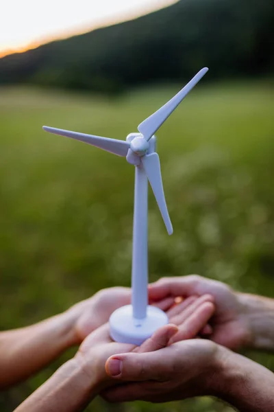 A close up of couple standing in nature with model of wind turbine. Concept of ecology future and renewable resources.