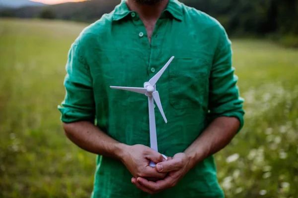 A close up of man standing in nature with model of wind turbine. Concept of ecology future and renewable resources.