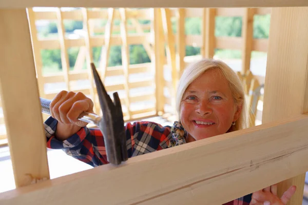Senior woman working inside of her unfinished ecological renewable low energy sustainable wooden eco house. Concept of active independent women and seniors, eco house and healthy lifestyle.
