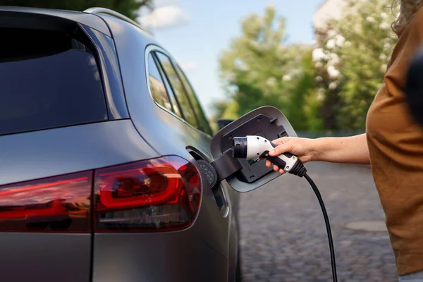 A woman holding power supply cable at electric vehicle charging station, closeup