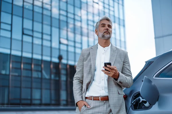 Businessman Holding Smartphone While Charging Car Electric Vehicle Charging Station — 스톡 사진