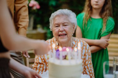 Büyükannenin doğum gününü kutlamak, açık hava aile bahçesi partisi mumlu bir pasta..