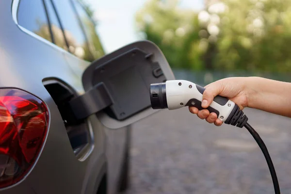 A woman holding power supply cable at electric vehicle charging station, closeup