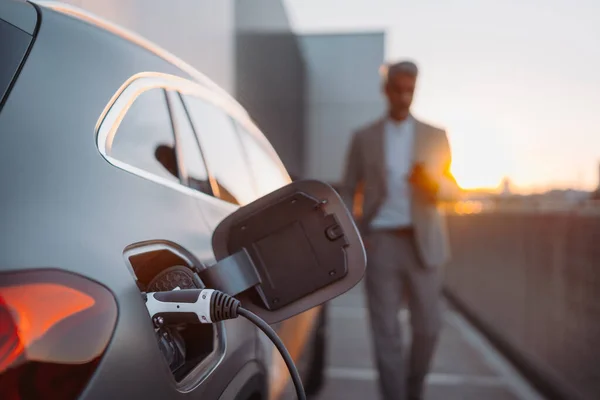 電気自動車の充電の終わり ビジネスマンの背景に立って待っている — ストック写真