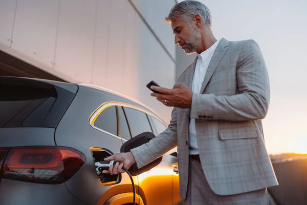 Businessman Holding Smartphone While Charging Car Electric Vehicle Charging Station — ストック写真