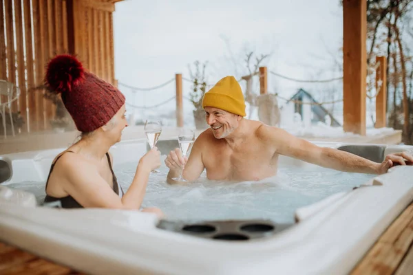 在寒冷的冬日里 头戴火帽的老夫妇在阳台上一起享受户外浴缸和碰杯的乐趣 — 图库照片