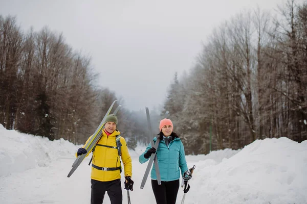 Pareja Mayor Cruzando Bosque Invierno Con Esquís Hombros —  Fotos de Stock