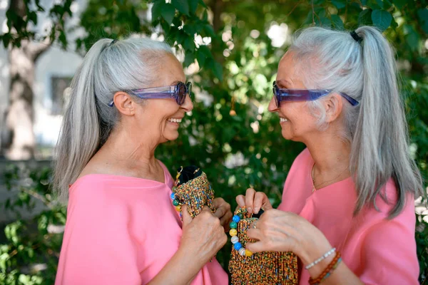 Portrait of a senior women twins looking each other outdoor, side view.
