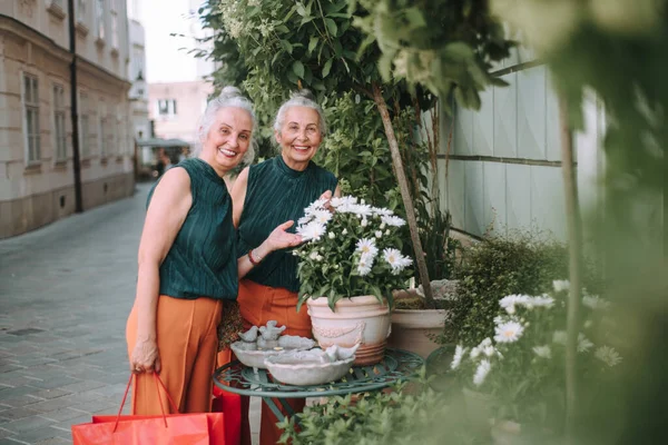 Ηλικιωμένες Γυναίκες Δίδυμα Περπατούν Μια Πόλη Και Ποζάρουν Κοντά Λουλούδια — Φωτογραφία Αρχείου