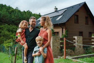 Evlerinin yanında güneş panelleri olan mutlu bir aile. Alternatif enerji, tasarruf kaynakları ve sürdürülebilir yaşam tarzı kavramı.