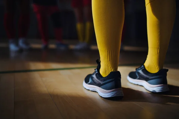 Close-up of womans legs in knee socks and trainers in front of football mach in gym.