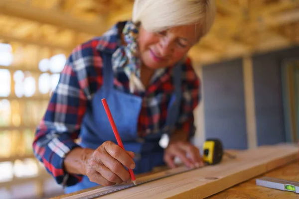 一位老年妇女在她未完工的生态木房子里测量木板 — 图库照片