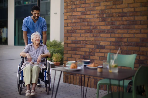 Vårdgivare Tar Sin Senior Klient Rullstol Vid Frukost Utomhus Staden — Stockfoto