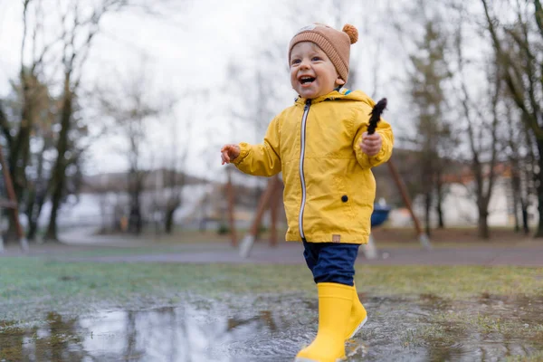 Šťastný Chlapeček Žlutém Plášti Skákání Kaluži Hraní Jehličnanem Dešti — Stock fotografie