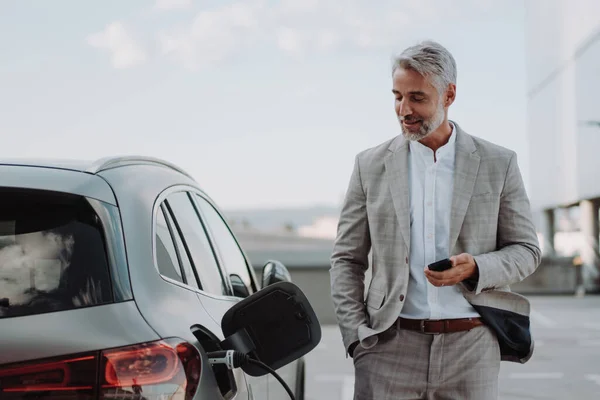 Businessman Holding Smartphone While Charging Car Electric Vehicle Charging Station — 스톡 사진