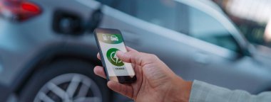 Elektirikli aracını şarj istasyonunda şarj etmek için telefon uygulaması kuran adam, yakın plan..