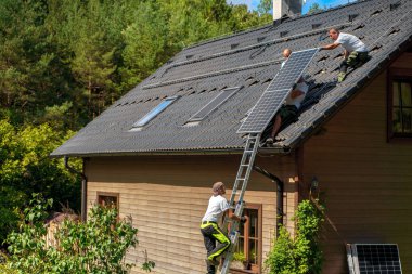 Çatıya güneş fotovoltaik panelleri, alternatif enerji, tasarruf kaynakları ve sürdürülebilir yaşam tarzı konsepti kuran erkek işçiler.
