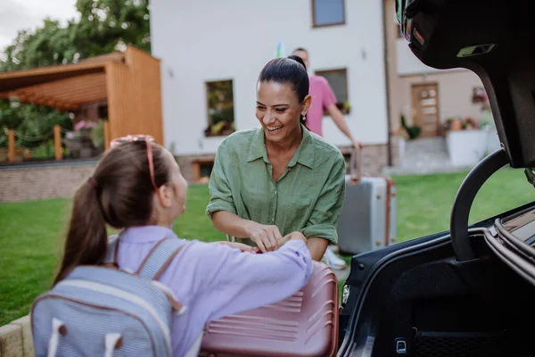 車のトランクにスーツケースを入れて休暇の準備をしている幸せな家族電気自動車の充電中に — ストック写真