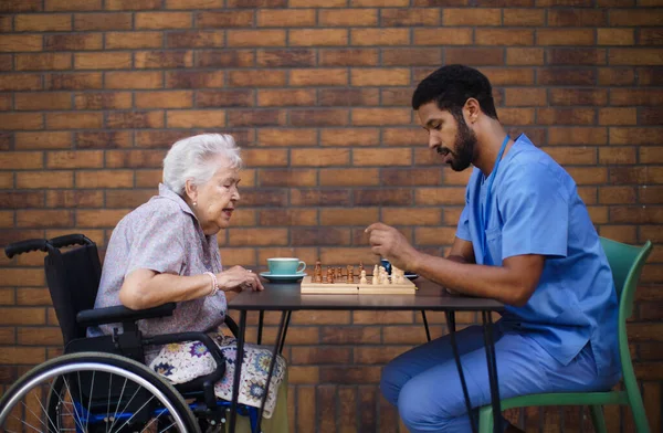 Vårdgivare Spelar Schack Och Dricker Kaffe Med Sin Klient Utomhus — Stockfoto