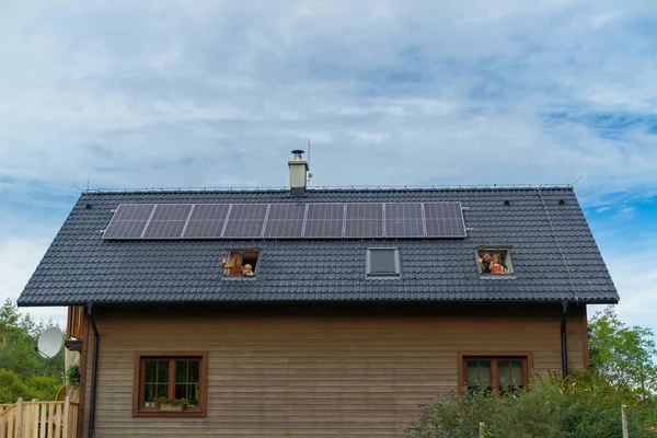 屋根の上にソーラーパネルが設置された家の窓からは幸せな家族が手を振っています 代替エネルギー 省資源 持続可能なライフスタイルの概念 — ストック写真