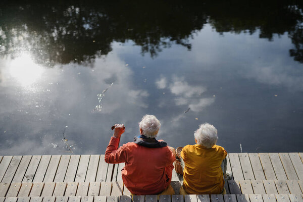 Happy senior couple at autumn walk near a lake, having break,sitting at pier.