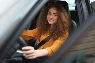 A young woman driving a car in the city. Portrait of a beautiful woman in a car, looking out of the window and smiling.