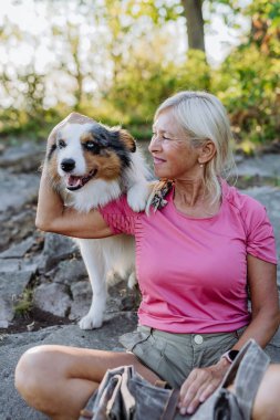 Yaşlı kadın ormanda yürürken dinleniyor ve köpeğini okşuyor..