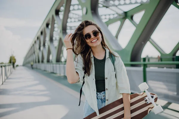 スケートボードで街の橋を歩く若い女性 若者文化と通勤概念 — ストック写真