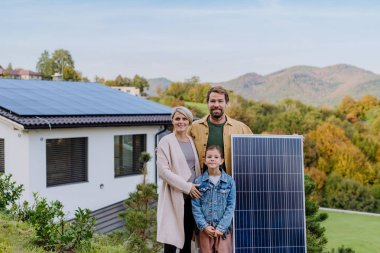 Evlerinin yakınında güneş paneli olan mutlu bir aile. Alternatif enerji, tasarruf kaynakları ve sürdürülebilir yaşam tarzı kavramı.