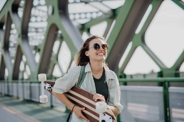 带着滑板走在城市桥上的年轻女子 青年文化和通勤概念 — 图库照片