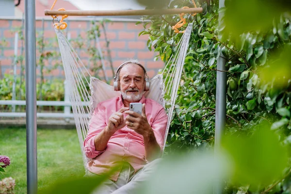 Heureux Homme Âgé Assis Dans Balançoire Jardin Avec Écouteurs Smartphone — Photo