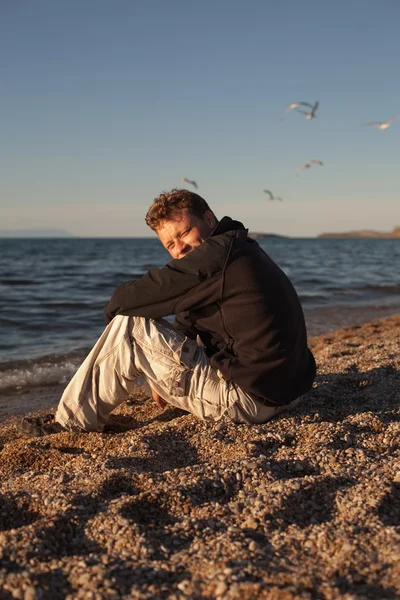 Jeune homme assis sur la plage — Photo