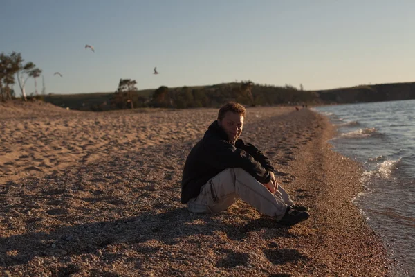 Junger Mann sitzt am Strand — Stockfoto