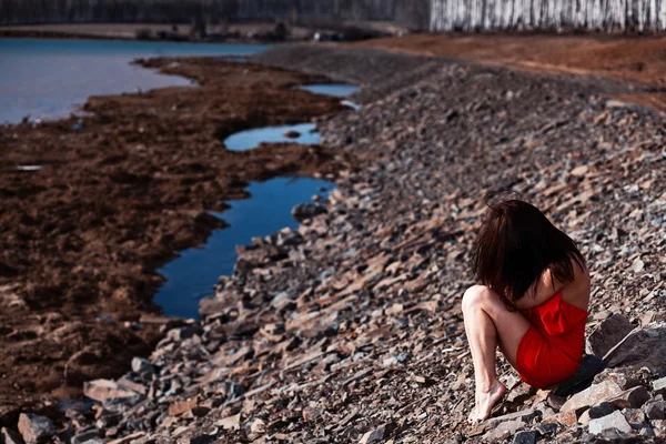 Young woman sitting on the beach in a red dress — Stock Photo, Image