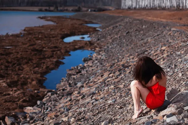 年轻女子坐在一件红色连衣裙的海滩上 — 图库照片