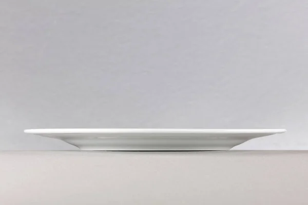 Side view of a white dinner plate on neutral background —  Fotos de Stock