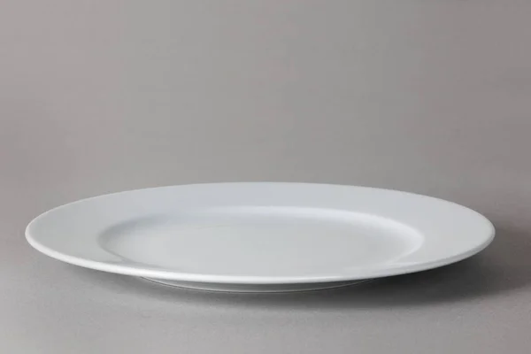 Flat front angle view of a white dinner plate on neutral background with shadow —  Fotos de Stock